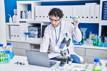 Young hispanic man scientist using laptop holding test tube at laboratory
