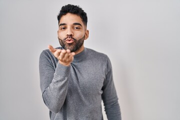 Hispanic man with beard standing over white background looking at the camera blowing a kiss with hand on air being lovely and sexy. love expression.