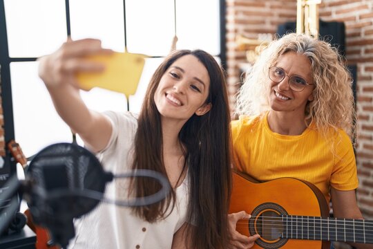 Two women musicians playing classical guitar making selfie by smartphone at music studio
