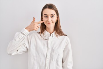 Young caucasian woman standing over isolated background pointing with hand finger to face and nose, smiling cheerful. beauty concept