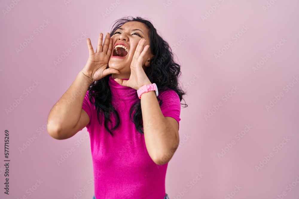 Poster young asian woman standing over pink background shouting angry out loud with hands over mouth