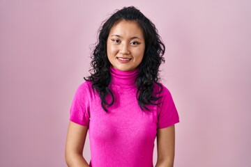 Young asian woman standing over pink background with hands together and crossed fingers smiling relaxed and cheerful. success and optimistic