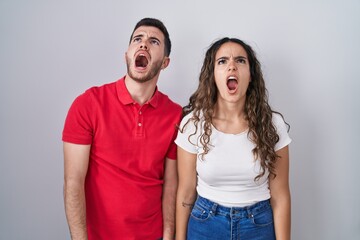 Young hispanic couple standing over isolated background angry and mad screaming frustrated and furious, shouting with anger. rage and aggressive concept.