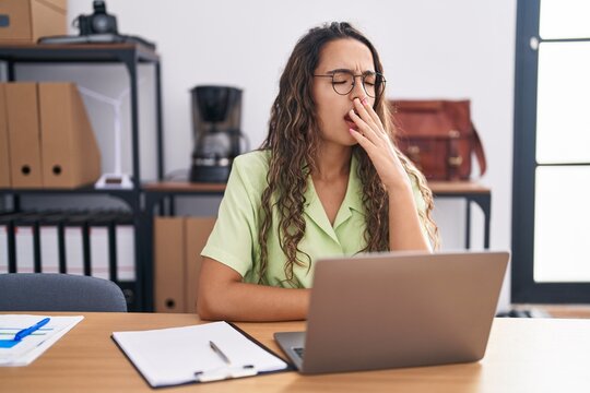 Young hispanic woman working at the office wearing glasses bored yawning tired covering mouth with hand. restless and sleepiness.