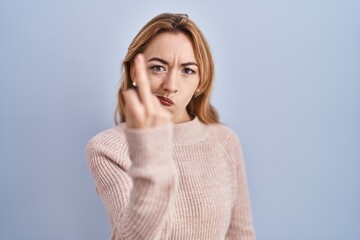 Hispanic woman standing over blue background showing middle finger, impolite and rude fuck off expression