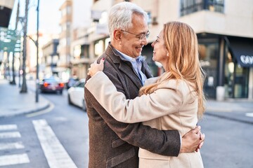 Fototapeta premium Middle age man and woman couple hugging each other standing at street