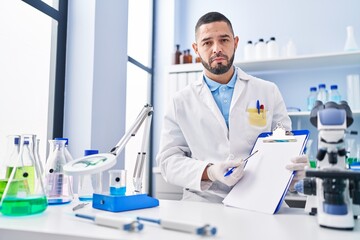 Hispanic man working at scientist laboratory holding blank clipboard depressed and worry for distress, crying angry and afraid. sad expression.