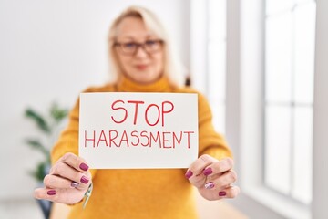 Middle age blonde woman business worker smiling confident holding stop harassement banner at office