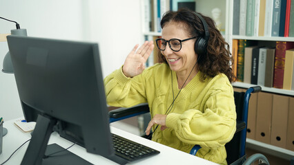 Middle age hispanic woman teacher having video call sitting on wheelchair at library university