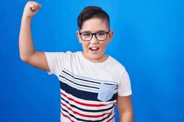 Young hispanic kid standing over blue background angry and mad raising fist frustrated and furious while shouting with anger. rage and aggressive concept.