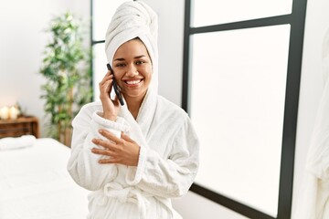 Young latin woman wearing bathrobe holding credit card at beauty center