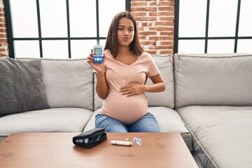 Young pregnant woman checking blood sugar puffing cheeks with funny face. mouth inflated with air, catching air. - obrazy, fototapety, plakaty