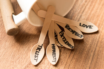 Bunch of  wooden spoons laying from a white coloured coffee mug each spoon hand written with words like love ,trust ,patience ,empathy ,honesty the essence of relationship in a wooden background