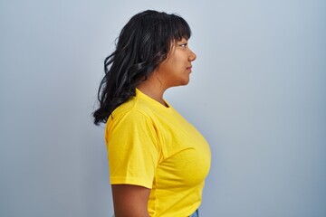 Hispanic woman standing over blue background looking to side, relax profile pose with natural face...