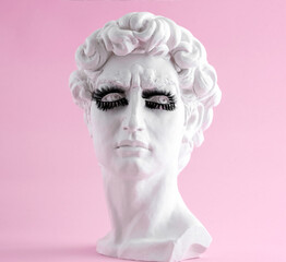 Plaster statue head wearing eyelashes pink background. Minimal art poster. Beauty procedure concept.