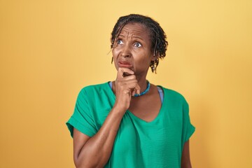 African woman with dreadlocks standing over yellow background thinking worried about a question,...