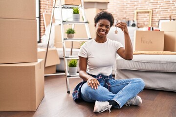 African american woman holding key sitting on floor at new home