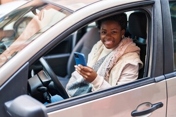 African american woman using smartphone sitting on car at street
