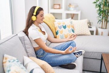 Young hispanic woman doing yoga exercise sitting on sofa at home