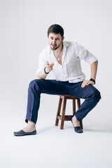 Portrait of a handsome man with a beard in a white shirt sits on a chair