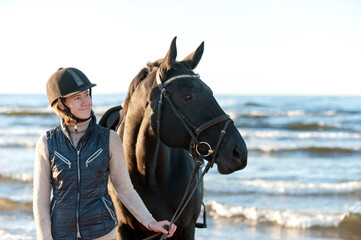 Young smiling Lady standing together with horse on sea beach