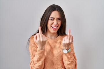 Young brunette woman standing over white background showing middle finger doing fuck you bad...