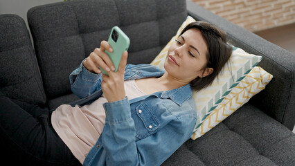 Young caucasian woman using smartphone lying on sofa at home - obrazy, fototapety, plakaty
