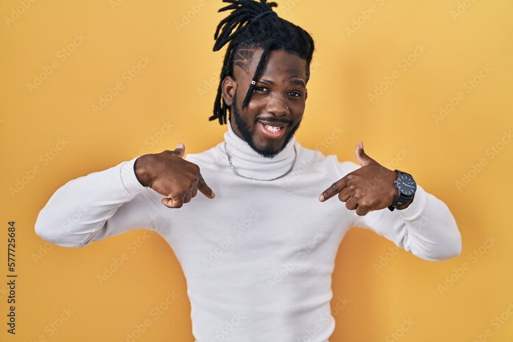 Poster African man with dreadlocks wearing turtleneck sweater over yellow background looking confident with smile on face, pointing oneself with fingers proud and happy.