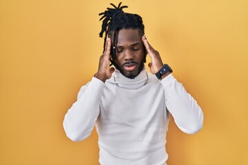 African man with dreadlocks wearing turtleneck sweater over yellow background with hand on head, headache because stress. suffering migraine.