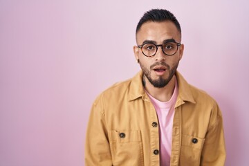 Young hispanic man standing over pink background afraid and shocked with surprise expression, fear and excited face.