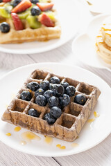 Belgian waffles with fruits berries and honey maple syrup set on white cafe table.