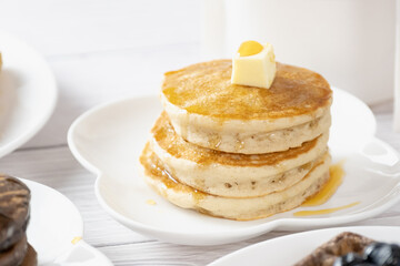 Pancake with butter and honey maple syrup set on white cafe table.