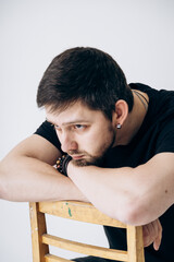 Obraz premium A guy in a black T-shirt sits on a chair and is sad. male portrait