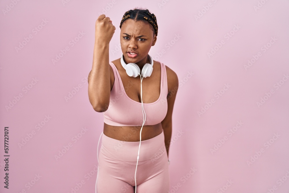 Canvas Prints African american woman with braids wearing sportswear and headphones angry and mad raising fist frustrated and furious while shouting with anger. rage and aggressive concept.