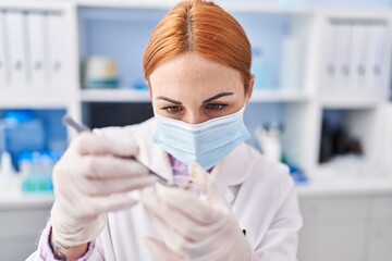 Young caucasian woman scientist wearing medical mask holding sample with tweezer at laboratory
