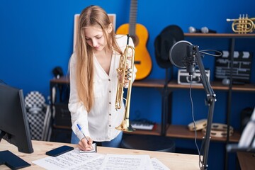Young caucasian woman musician composing song holding trumpet at music studio