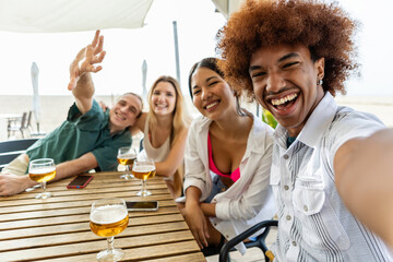 Happy group of diverse young friends enjoying summer vacation together taking selfie portrait at beach bar