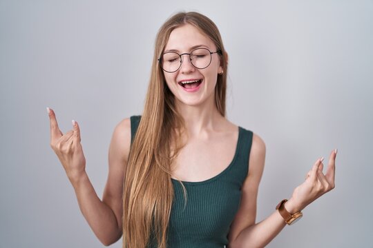 Young caucasian woman standing over white background shouting with crazy expression doing rock symbol with hands up. music star. heavy music concept.