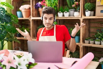 Young hispanic man working at florist shop doing video call shouting and screaming loud to side with hand on mouth. communication concept.