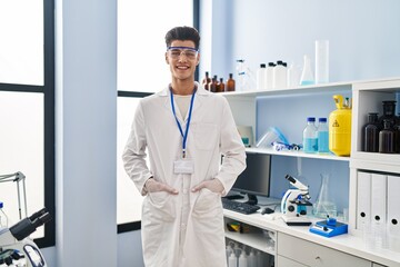 Young hispanic man wearing scientist uniform standing at laboratory