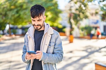 Fototapeta premium Young hispanic man smiling confident using smartphone at park