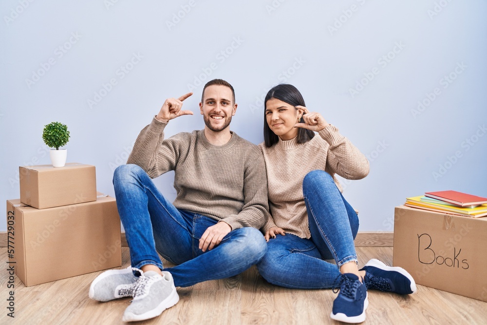 Canvas Prints Young couple moving to a new home smiling and confident gesturing with hand doing small size sign with fingers looking and the camera. measure concept.