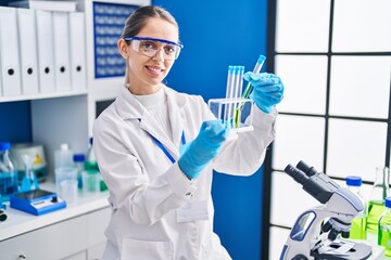 Young woman scientist smiling confident holding test tubes at laboratory