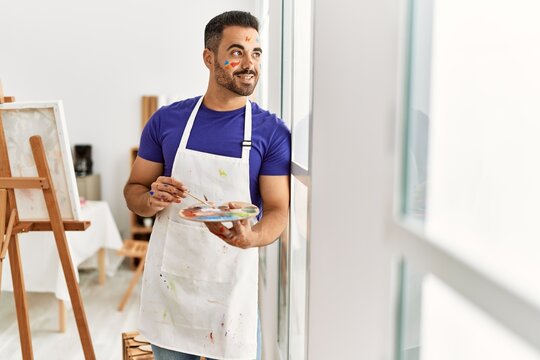 Young hispanic man smiling confident mixing color on palette at art studio