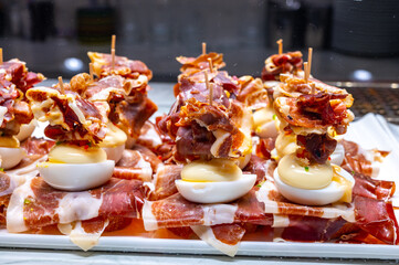 Fototapeta na wymiar Typical snack of Basque Country, pinchos or pinxtos, small piece of bread on skewers with egg, jamon and different toppings, served in bar in San-Sebastian or Bilbao, Spain