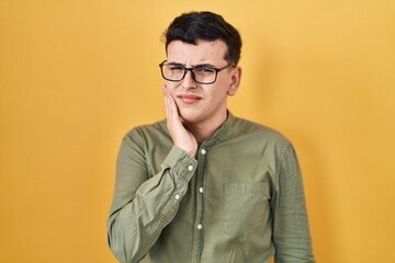Non binary person standing over yellow background touching mouth with hand with painful expression because of toothache or dental illness on teeth. dentist