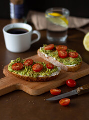 Toast with avocado and cherry tomatoes on a wooden board