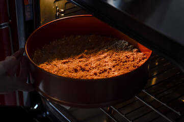 hands inserting the pan with the mix of biscuit crumbs, sugar and butter into the oven to bake the base of a cheesecak