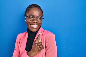 Beautiful black woman standing over blue background cheerful with a smile of face pointing with...