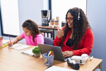 Mother and young daughter at the office working and doing homework pointing thumb up to the side smiling happy with open mouth
